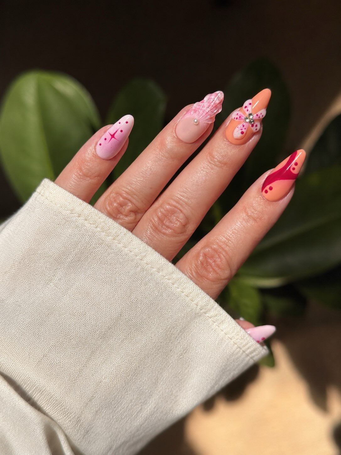 Manicura artística con flor 3D, alas de mariposa y detalles en tonos coral y rosa